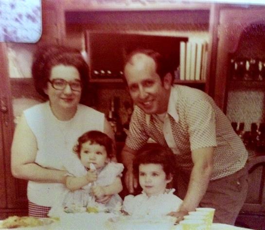 Parents smile as they gather with their two young daughters at home, creating a warm family moment.
