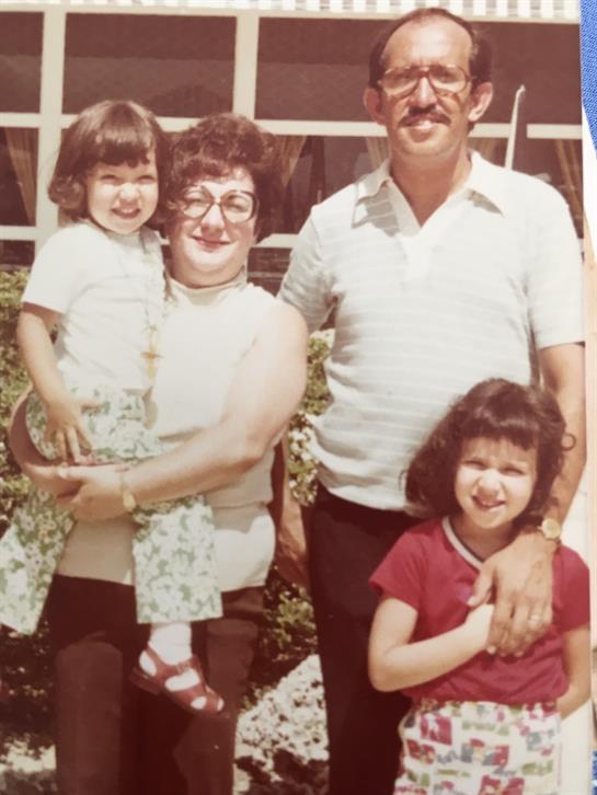 A joyful family stands together outside, with children being held by their grandmother.