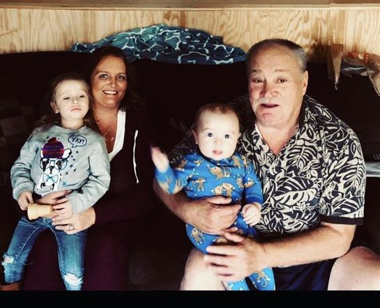 A happy family poses on a couch, with two kids smiling and waving at the camera.