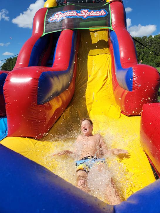 A young child enjoys a thrilling ride down a bright water slide, splashing into the pool below.
