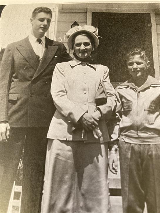 Three individuals pose together, showcasing traditional clothing in a historical setting.
