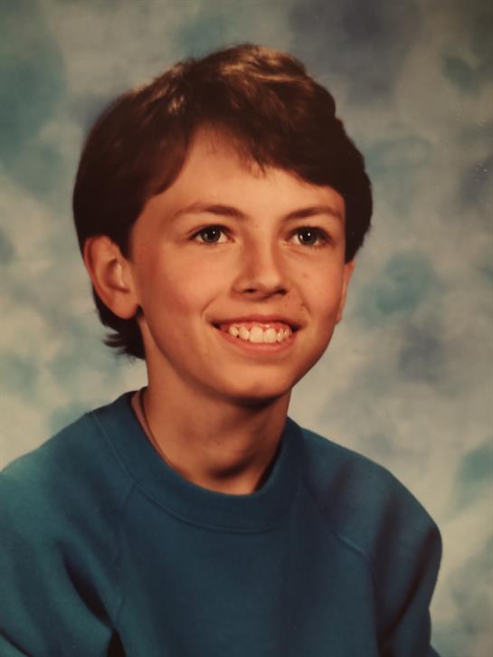 A boy smiles confidently in a school portrait, wearing a blue sweatshirt.