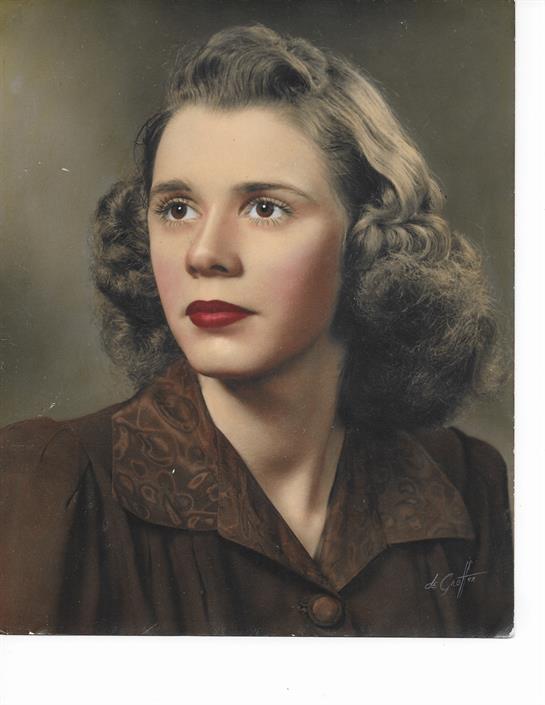 A young woman with curly hair and red lips poses gracefully in a vintage-style studio.