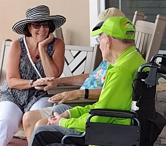 Residents are gathered on a porch, enjoying friendly conversation in the warm sun.