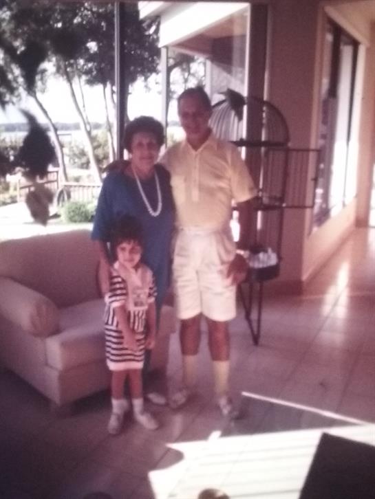 Three people, including a child, smile while standing together in a bright room with plants.