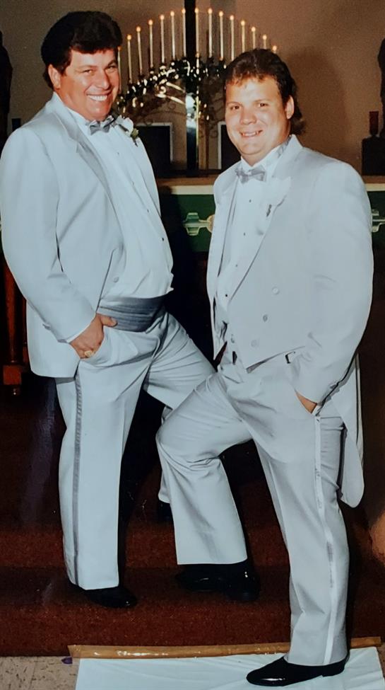 Two men stand confidently in light gray tuxedos, showcasing style and camaraderie at a celebration.