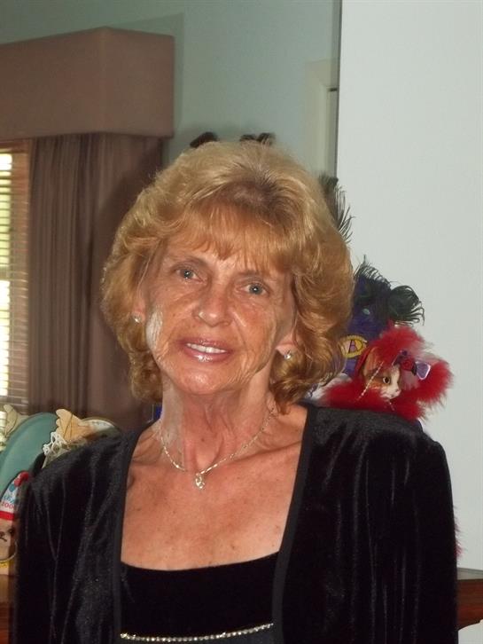 A woman smiles brightly while dressed elegantly for a gathering in a comfortable, decorated room.