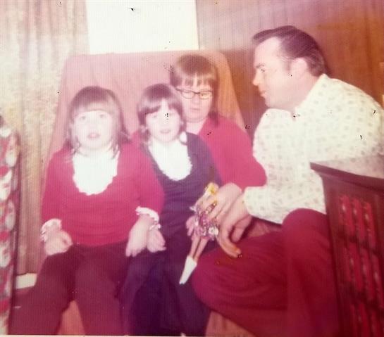 Two children sit excitedly with adults in a warm, inviting living room filled with nostalgia.