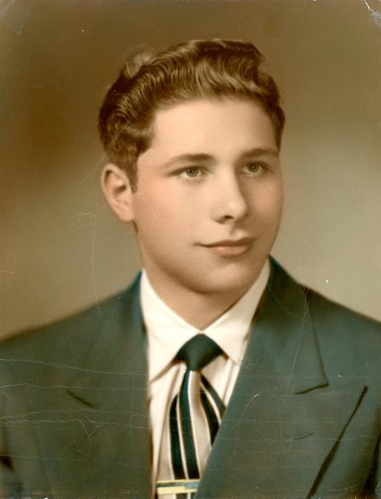 A well-dressed young man poses confidently in a suit and tie against a soft background.