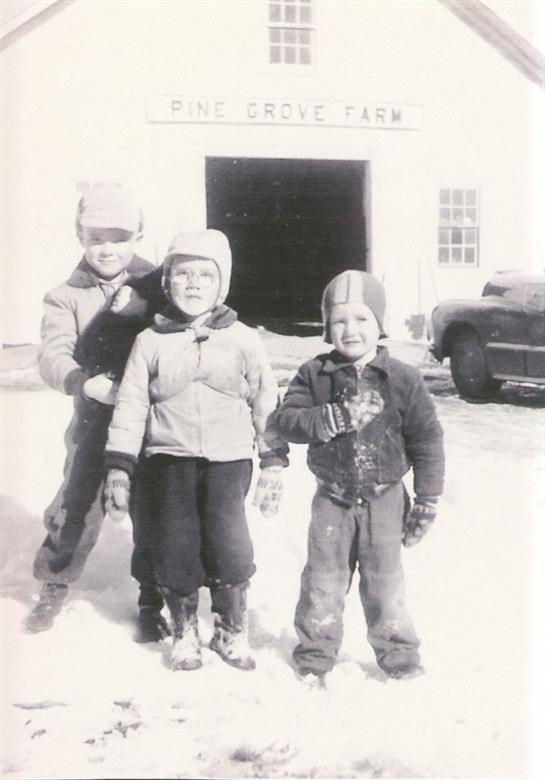 Three children enjoy a snowy day outside a building, smiling and dressed warmly for winter fun.