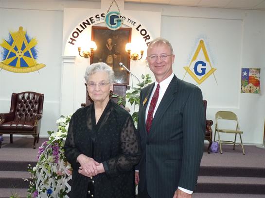 Two individuals stand together in formal clothing inside a church during a daytime gathering.