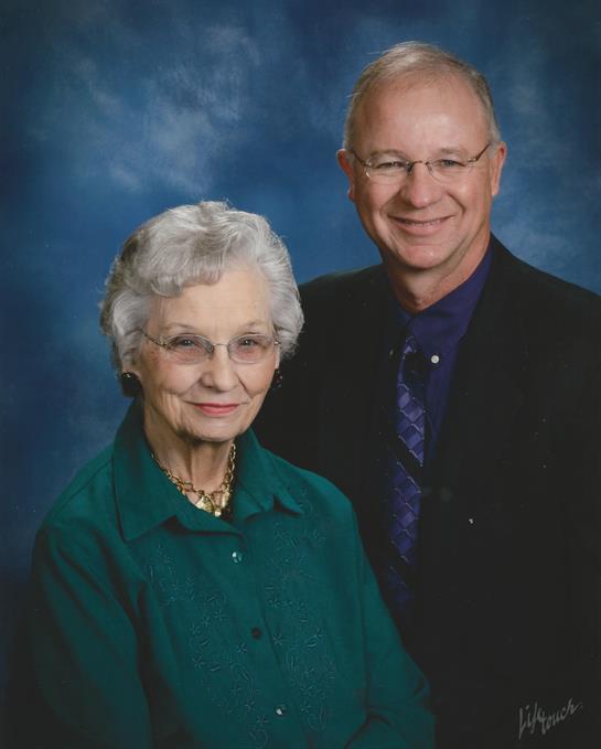 An elderly couple poses together in a studio with a blue background, displaying smiles and love.