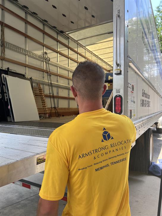 A worker in a yellow shirt is unloading items from a moving truck in a neighborhood.
