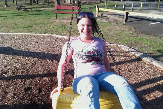 A woman is joyfully swinging on a playground swing, surrounded by greenery in a park.