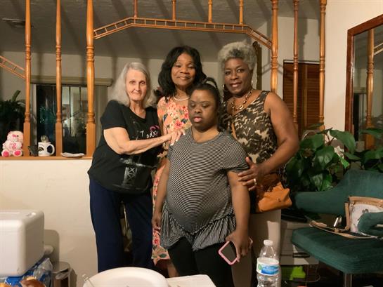 Four women smile together in a cozy living room, enjoying each other's company.