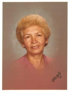 A senior woman with curled light blonde hair and a gentle smile is wearing a pink blouse.