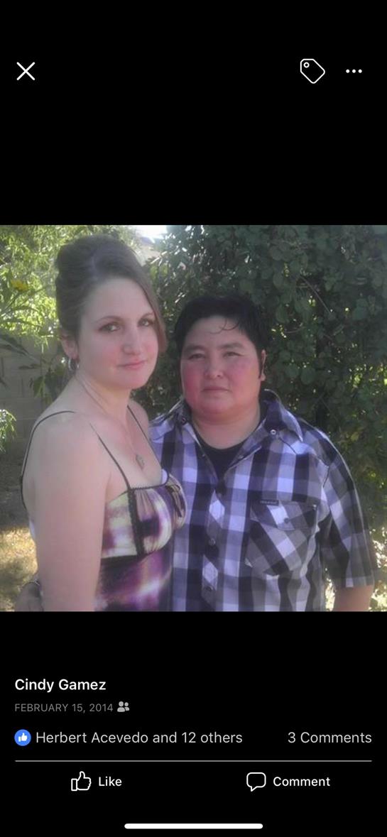 Two people stand closely together, smiling in a lush garden filled with greenery.