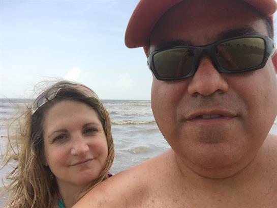 A couple stands in shallow water at the beach, enjoying a sunny day and each other's company.