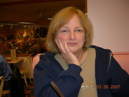 A woman in casual attire appears contemplative while seated at a table in a restaurant.