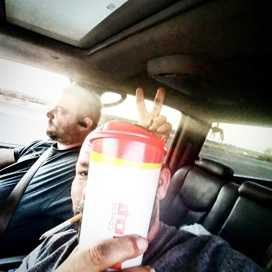 Friends are on a road trip, with one driving and the other happily taking a selfie.