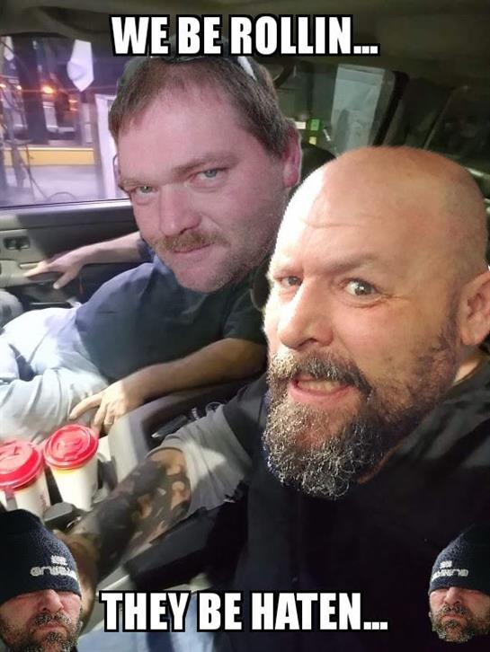 Two men smile for a selfie, seated in a vehicle, enjoying coffee in a city setting at night.