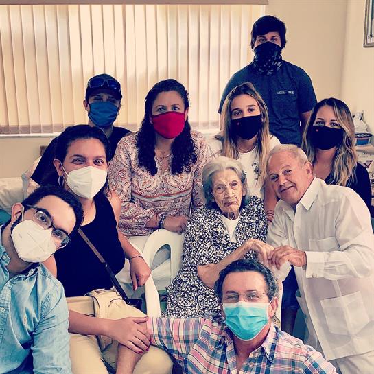 A joyful family gathers indoors, wearing masks and smiling, celebrating together.