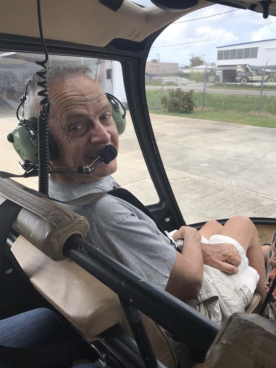 A joyful senior man sits in a helicopter cockpit, ready for takeoff and wearing a headset.