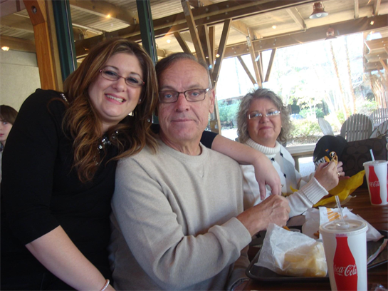 Three people enjoy lunch together at a lively restaurant on a warm day with bright sunshine.