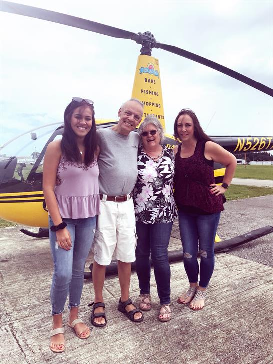 Four people enjoy a moment together next to a helicopter in a picturesque outdoor setting.