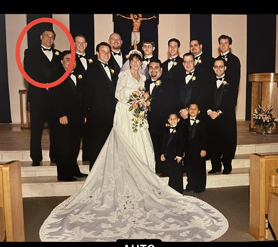 Bride and groom stand smiling among groomsmen and family members in a church setting.