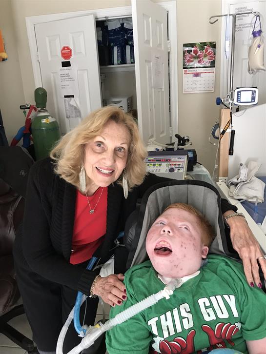 A caregiver smiles alongside a child in a wheelchair, creating a touching connection in therapy.