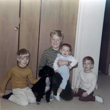 Siblings pose together with a black dog, showcasing joyful childhood moments indoors.
