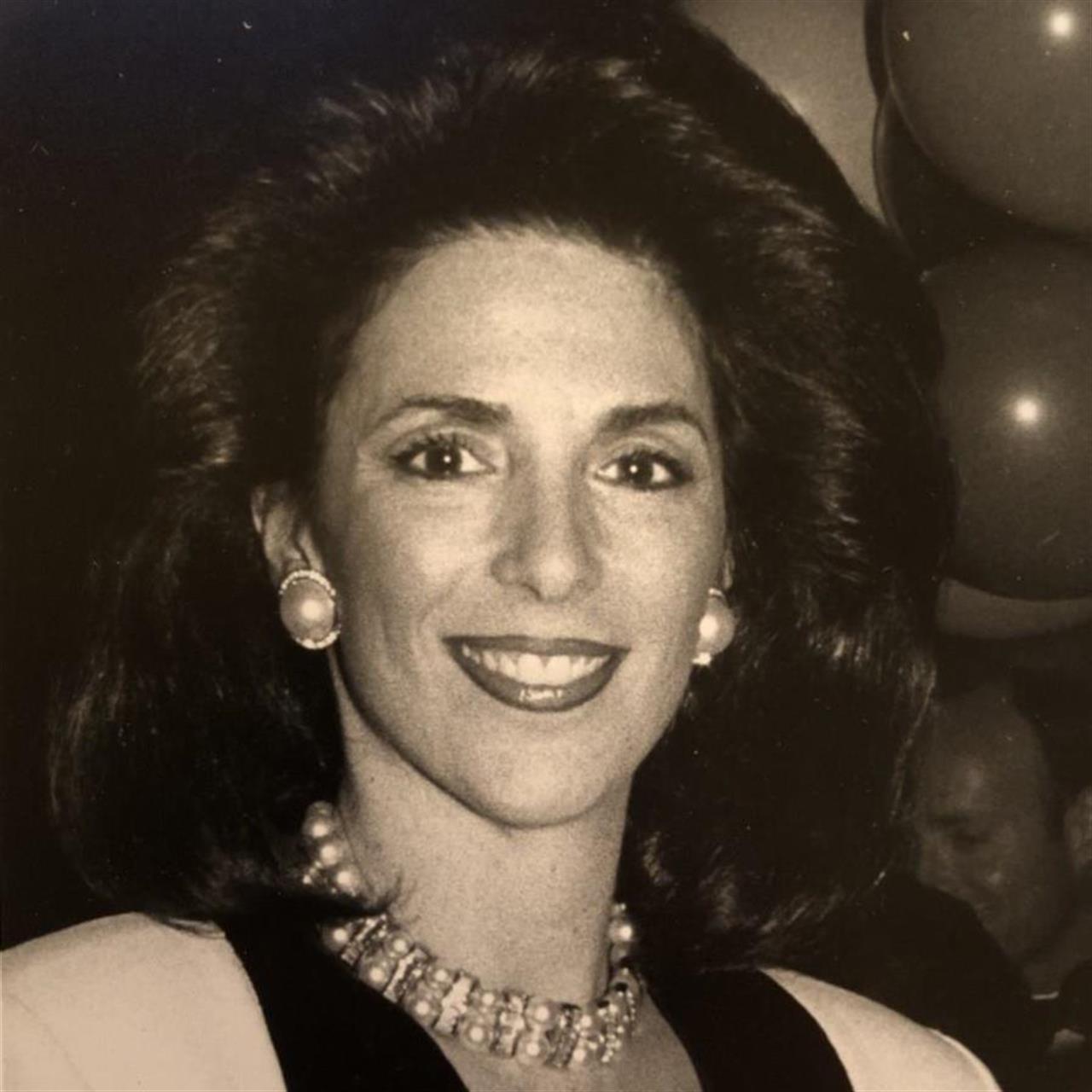 A woman stands in front of balloons and smiles at a gathering in the evening light.