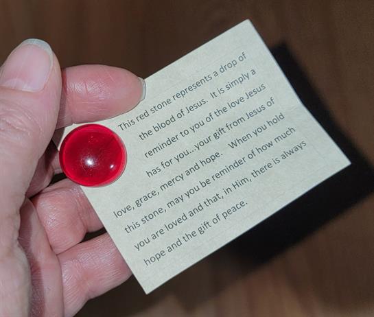 A hand holds a red stone with a note reminding of love, hope, and the importance of remembrance.