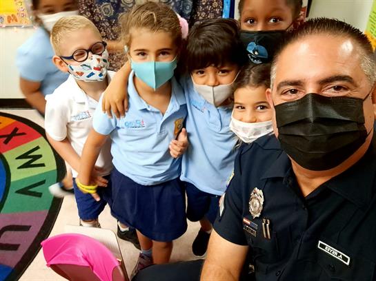 Young students and a police officer smile together in a classroom, sharing a cheerful moment.