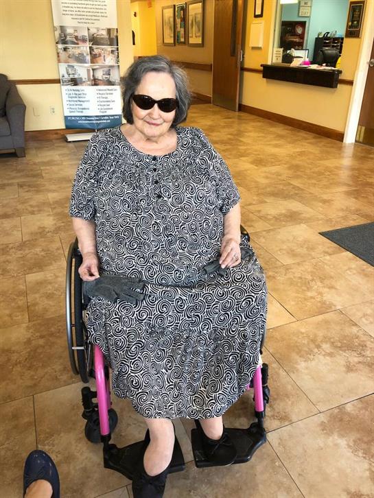 Elderly woman relaxes in a sunny lobby, enjoying her wheelchair and wearing sunglasses.