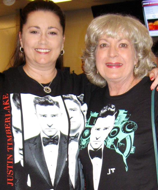 Two women share a joyful moment in matching shirts of a famous musician.
