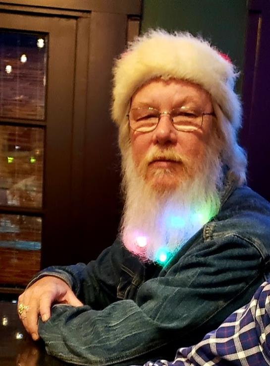 A man with a snowy beard and festive hat sits in a colorful cafe, enjoying the vibe.