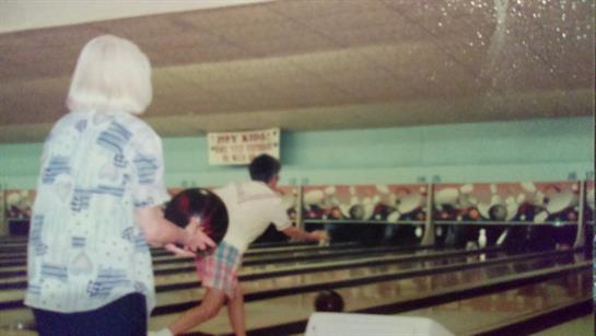 Bowlers roll balls as spectators cheer in a lively atmosphere.