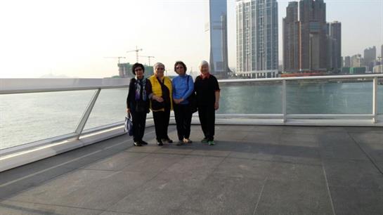 Four friends stand together at a waterfront promenade, enjoying the city view on a sunny day.