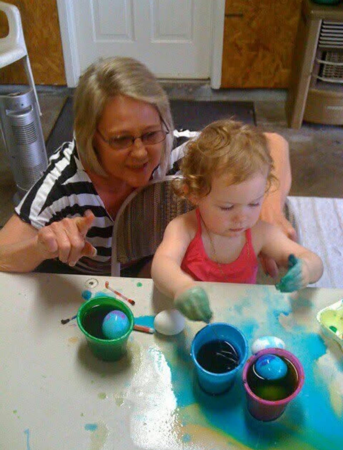A grandmother and her young granddaughter enjoy dyeing Easter eggs together with colorful paints.