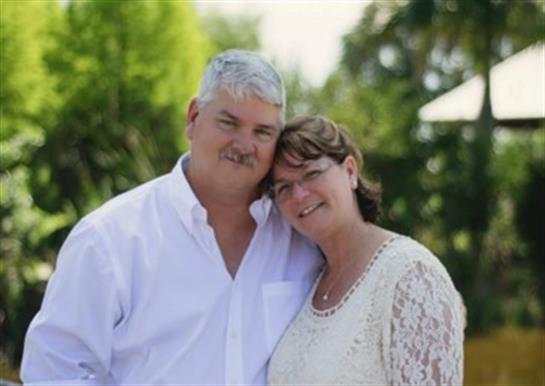 A cheerful couple stands close together in a beautiful garden, enjoying a joyful moment.