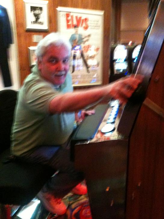 An older man smiles and plays with a vintage slot machine, adding to the lively atmosphere.