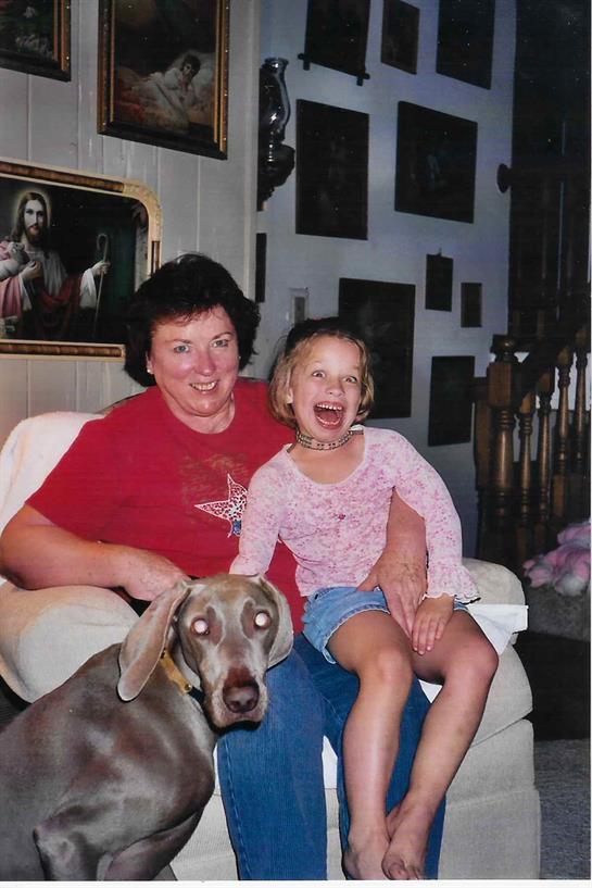 A woman and a young girl share a joyful moment while sitting on a couch with a dog.
