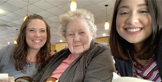 Three women, representing different generations, share smiles at a dining table during lunch.