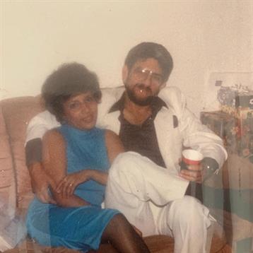 Two people sit close on a couch, sharing a casual moment in a relaxed indoor environment.