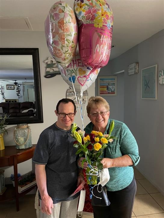 A person with Down syndrome and a woman celebrate Mother's Day with yellow roses and balloons.