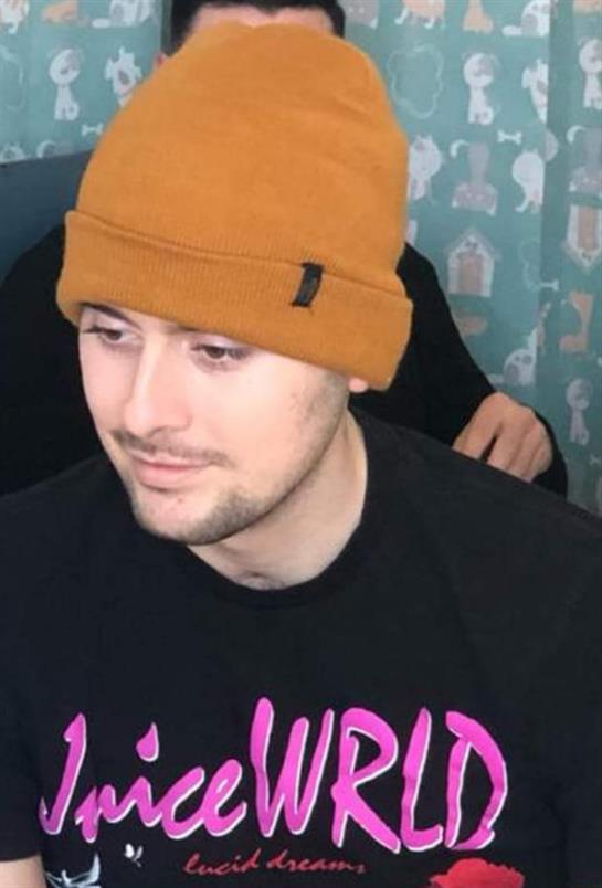 A young man with a brown beanie is talking with friends in a lively indoor space.