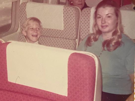 A young girl expresses joy while a woman sits calmly beside her on an airplane.
