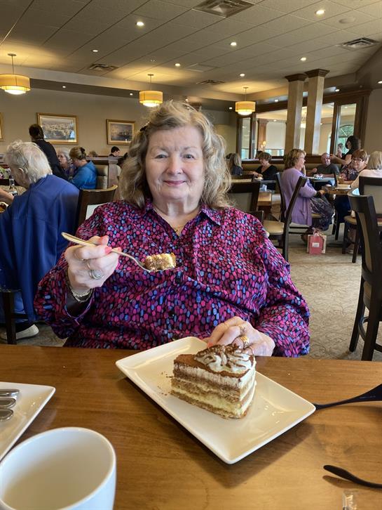 A happy elderly woman delights in a slice of cake while seated among friends.